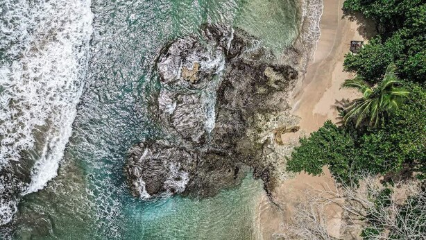 An aerial view of a beach with clear turquoise waters, rocky formations, and dense tropical vegetation. - Mini Up House · Romantic Caribbean Escape for 2 (Puerto Viejo de Talamanca)