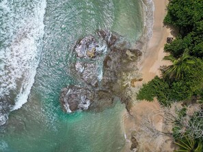 Una playa con agua turquesa cristalina, afloramientos rocosos y vegetación verde exuberante.