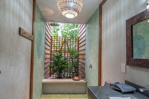 A bathroom with a shower, a sink, and a mirror. There are plants and a wooden lattice structure in the shower area.