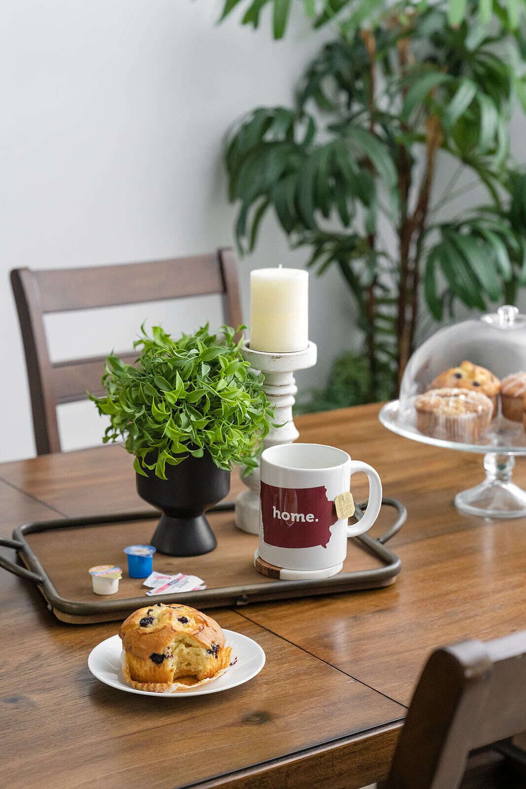 A dining table with a candle, a potted plant, a mug, and a plate with a muffin.