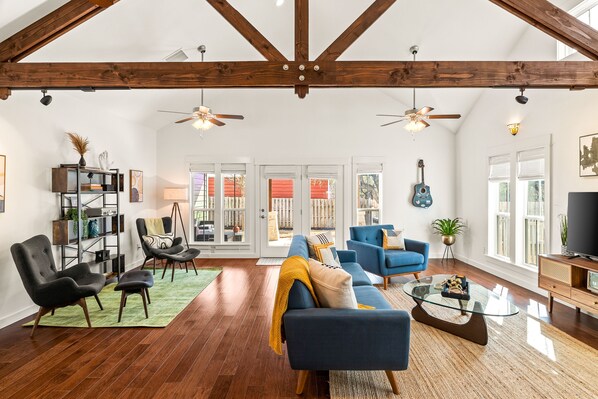 A spacious living room with a high ceiling, wooden beams, a blue sofa, a glass coffee table, and a bookshelf.