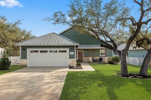 A two-story house with a green roof, a white garage, and a well-maintained lawn.