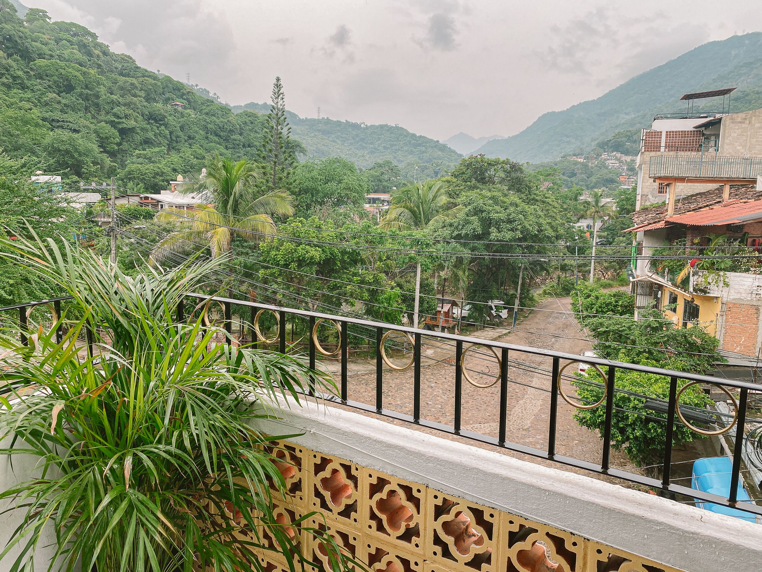 Un balcon offrant une vue sur une vallée verdoyante, une chaîne de montagnes lointaine et quelques bâtiments en arrière-plan.