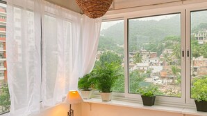 Een slaapkamer met een groot raam, een bed met een oranje sprei en uitzicht op een stadsbeeld.