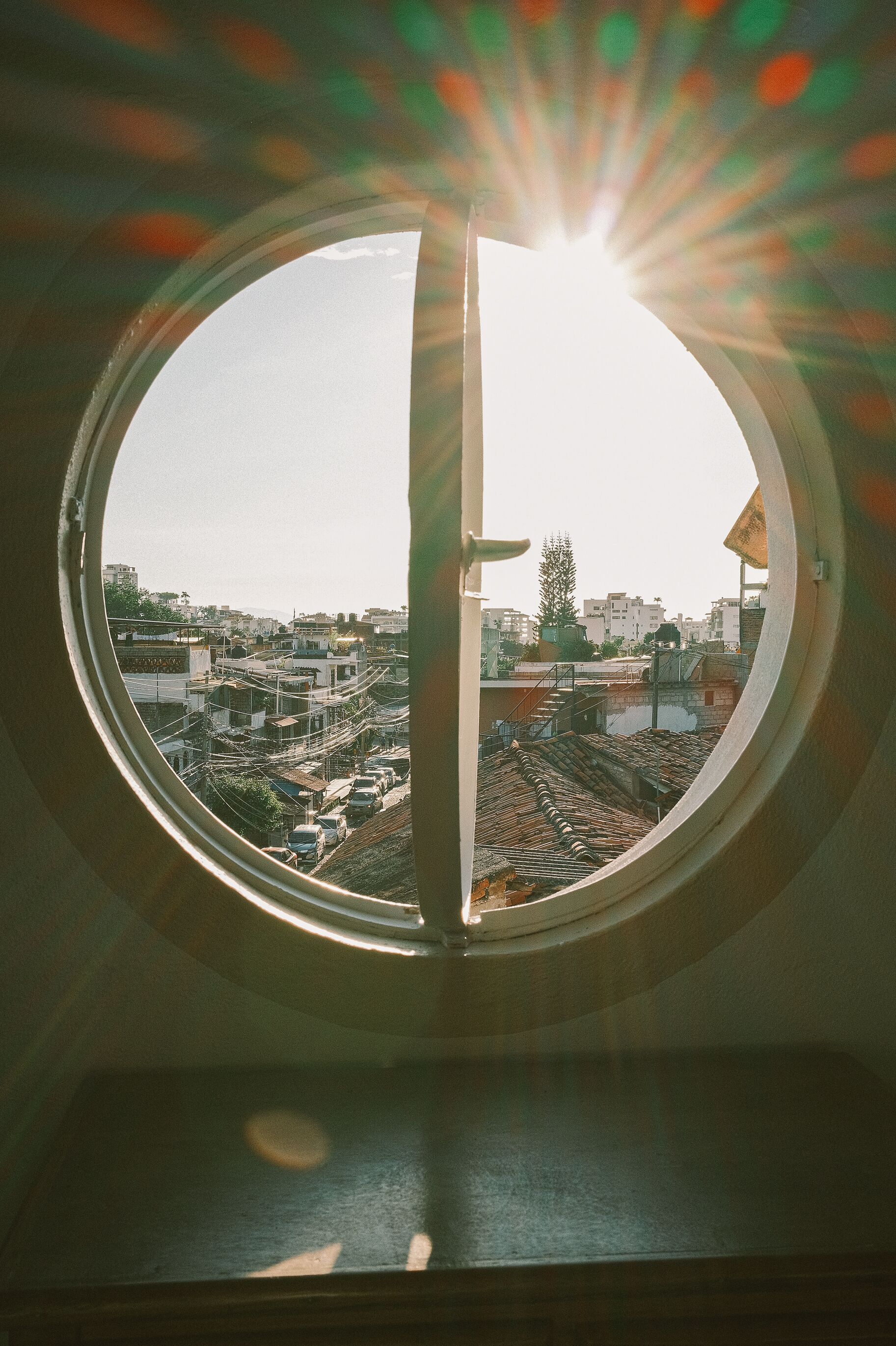 Ein rundes Fenster mit Blick auf eine Stadtansicht, darunter Gebäude und ein Baum.