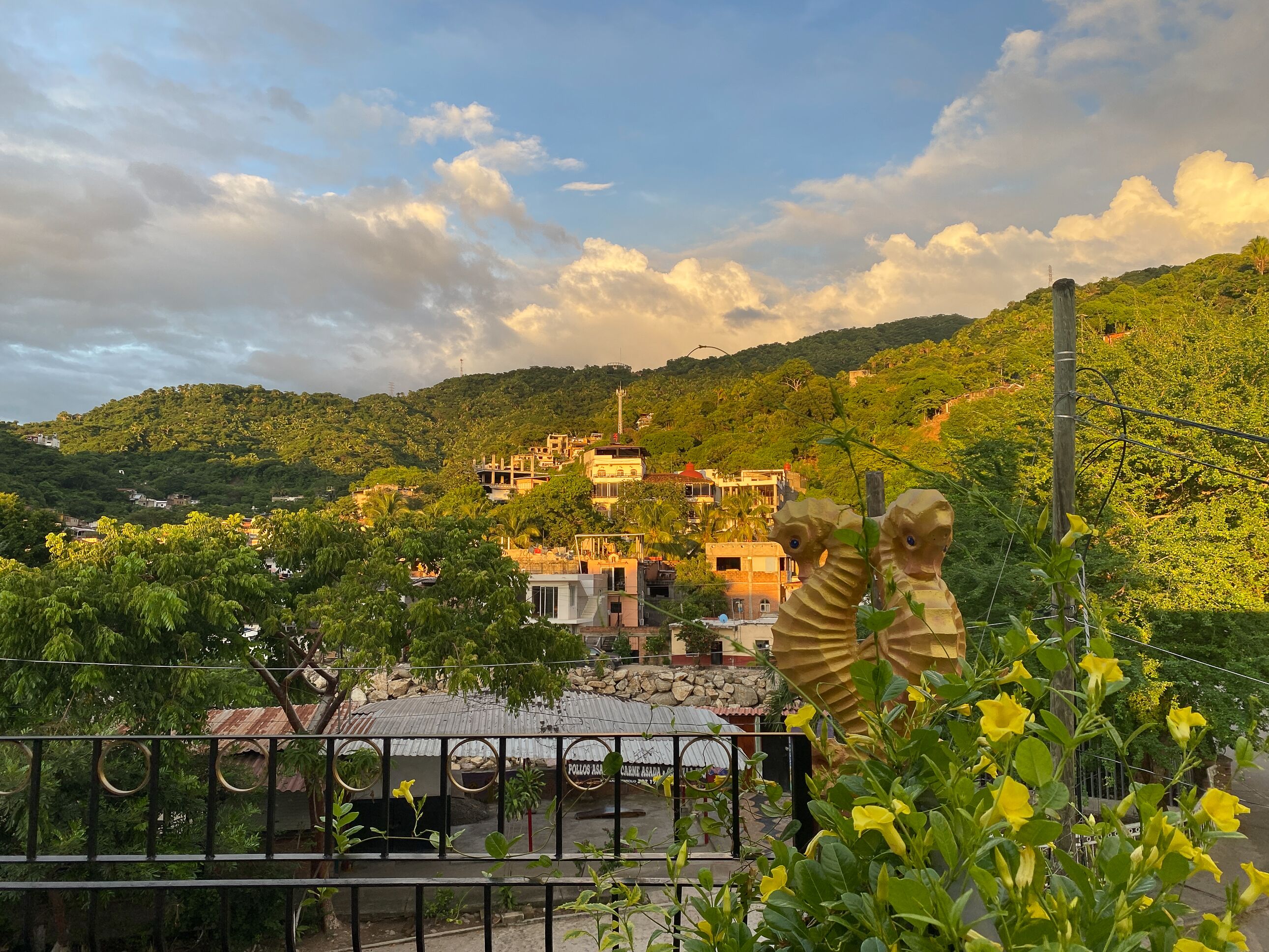 Un quartiere residenziale con case su una collina, una statua in primo piano e un cielo sereno.