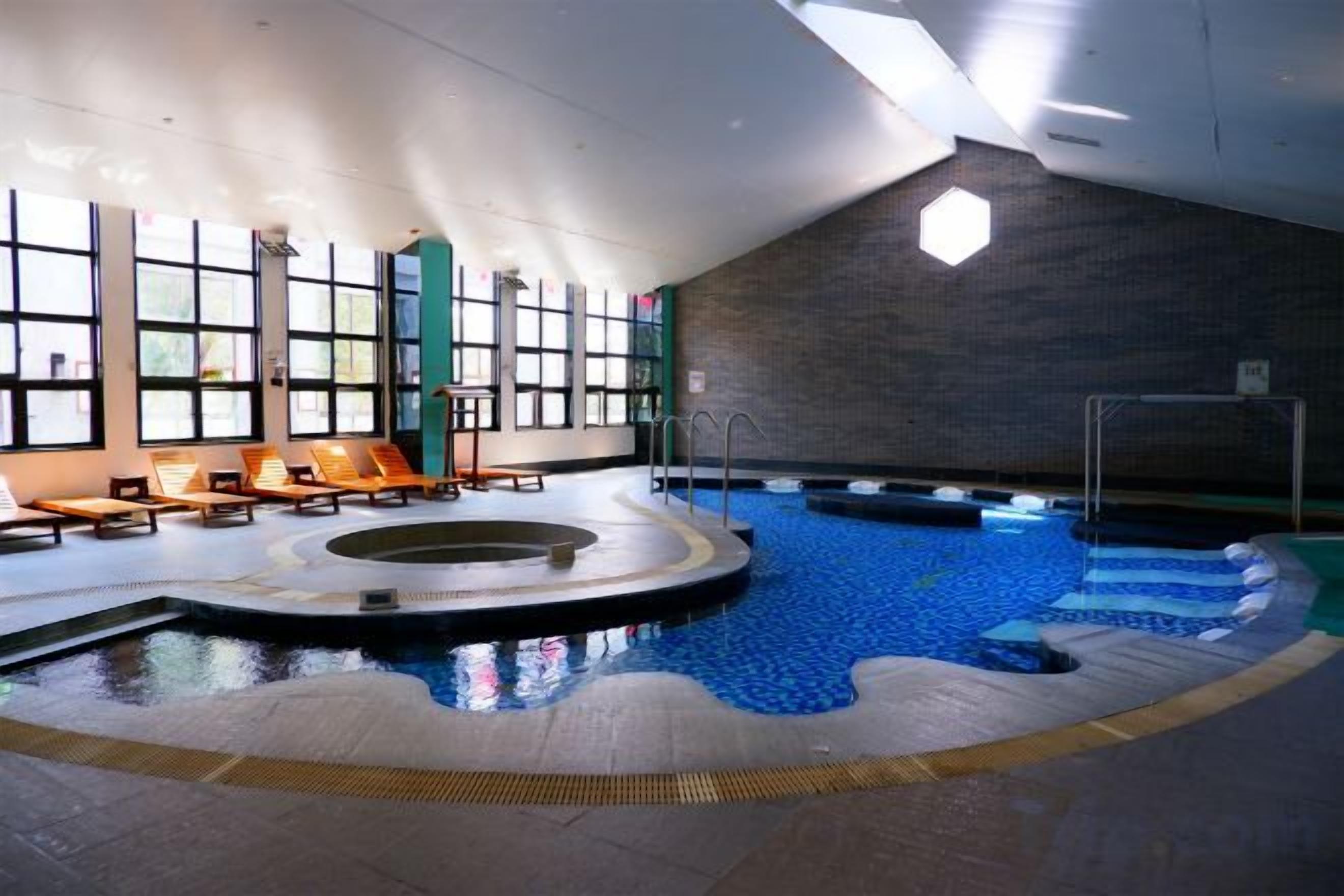 An indoor swimming pool with a sunlit area and lounge chairs.