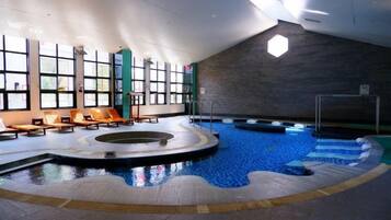 An indoor swimming pool with a sunlit area and lounge chairs.