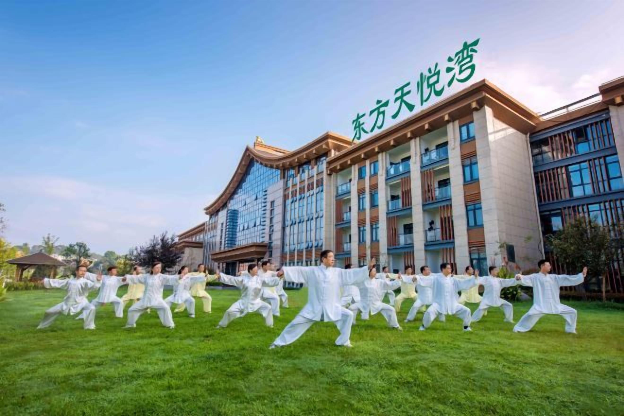 A group of people performing Tai Chi in front of a building with traditional and modern architectural elements.