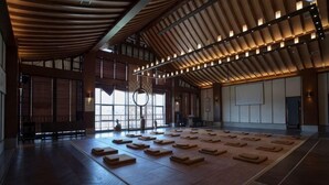 Un grand hall doté de tatamis, de poutres en bois et de grandes fenêtres.