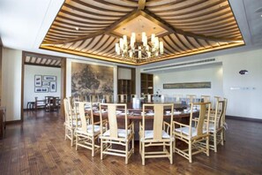 Un espace repas avec une table ronde entourée de chaises, un plafond en bois et un lustre.