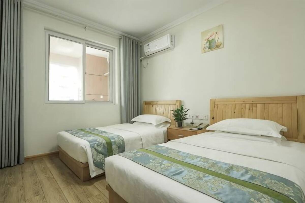 Een hotelkamer met twee bedden, een raam met gordijnen, een airconditioning en een kleine plant op het nachtkastje.