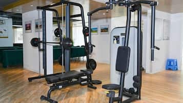 A gym with weightlifting equipment, a green table in the background, and a blue stool.