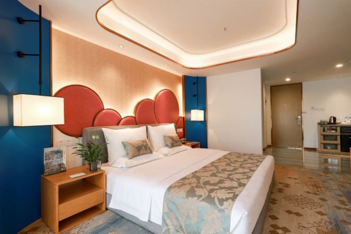 Une chambre d’hôtel moderne avec un grand lit, des tables de chevet, une petite table et une tête de lit décorative.
