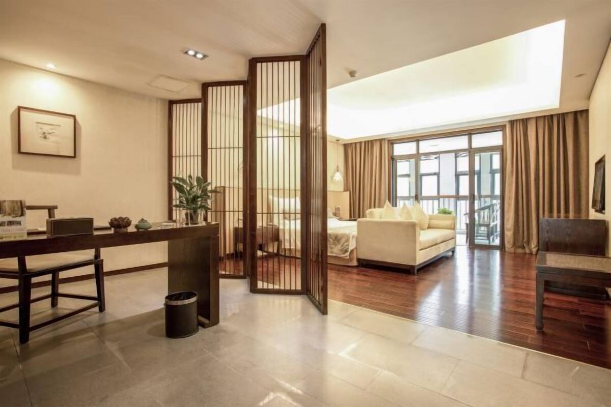 Een moderne hotelkamer met een houten scheidingswand, een bank, een eettafel en een groot raam.