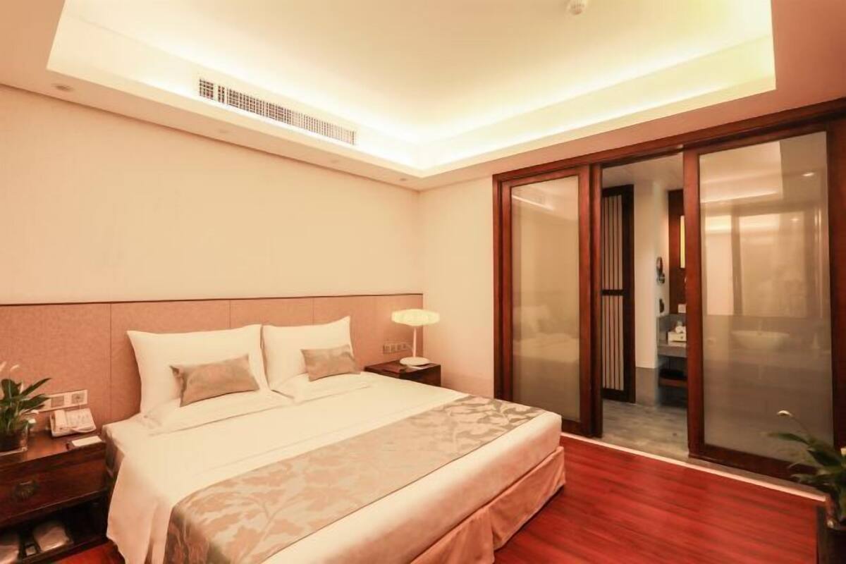 Een hotelkamer met een bed, nachtkastje, lamp en een schuifdeur naar een badkamer.
