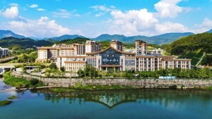 Un grand hôtel composé de plusieurs bâtiments, avec un plan d’eau aux reflets changeants à l’avant et des montagnes en arrière-plan.