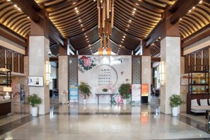 A spacious lobby with a high ceiling, a reception desk, and potted plants.