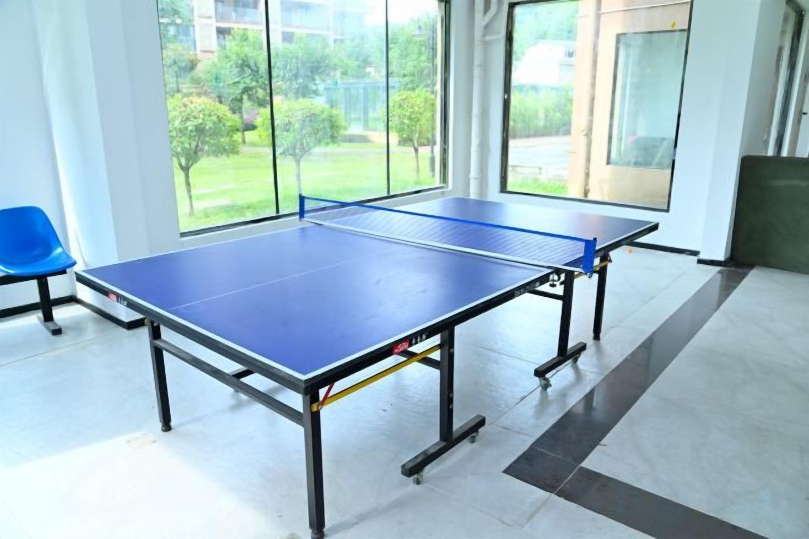 A ping pong table in a room with large windows, a blue chair, and a door leading outside.