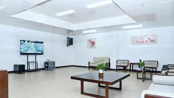 A spacious room with a large flat-screen TV, a wooden table, and several chairs.