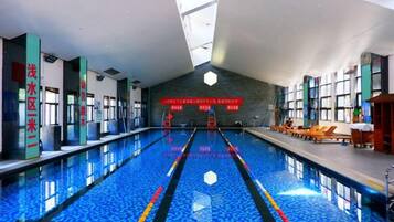 An indoor swimming pool with clear lane markings, a tiled floor, and a high ceiling with skylights.