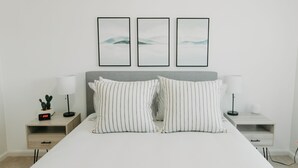 A neatly arranged bedroom with a bed, two bedside tables, a nightstand, a digital clock, and three framed pictures on the wall. - Spacious 3 BR House w/hot tub in SE Portland, Sleeps 8, near popular attractions (Wood Village)