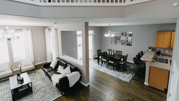 A spacious living area with a black leather sofa, a dining table with chairs, and a kitchen area with wooden cabinets. - Spacious 3 BR House w/hot tub in SE Portland, Sleeps 8, near popular attractions (Wood Village)