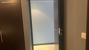 Een gang die leidt naar een kamer, met een deur, lichtschakelaar en een thermostaat op de muur.