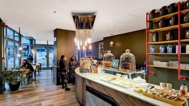 A modern cafe interior with wooden flooring, a central counter with food display, and shelves with packaged goods. - Lovely Relaxing-1 Bedroon 703 Condo (Cape Town)