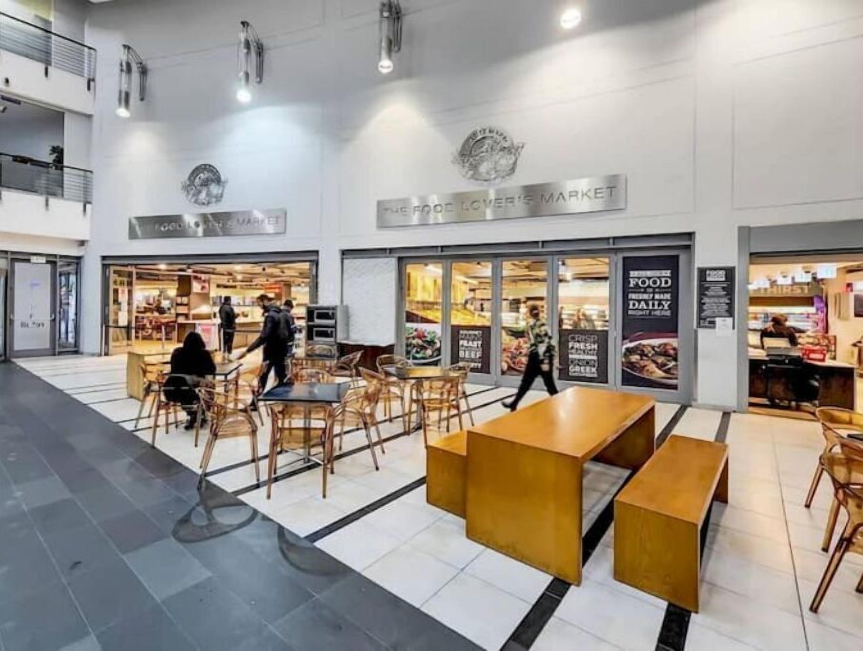 A food court with tables and chairs, a seating area with benches, and a sign for 'The Food Lover's Market'.