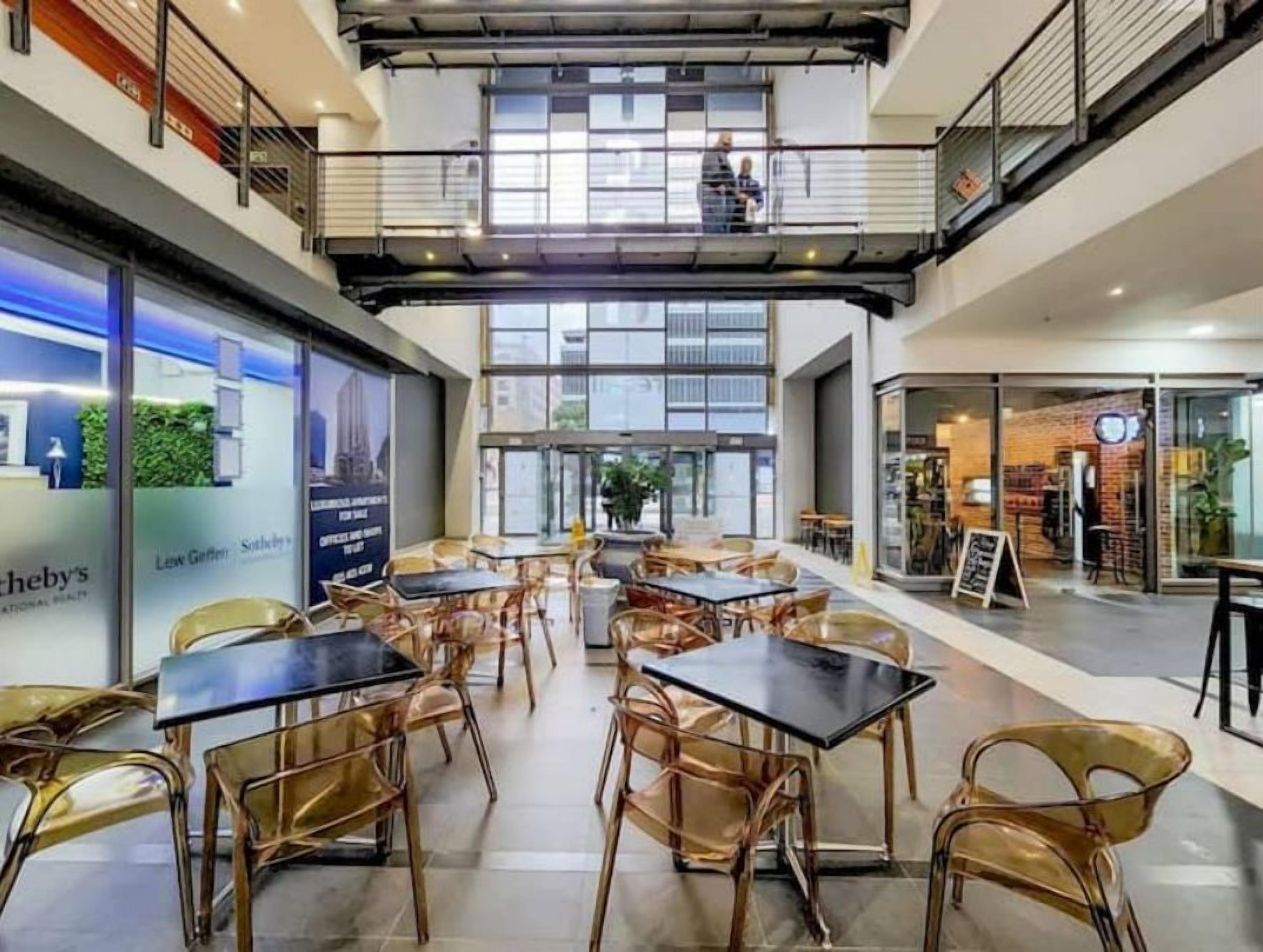 Amplio espacio interior con varias mesas y sillas, un entrepiso con barandilla y ventanas grandes que permiten la entrada de luz natural.
