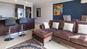 Uma sala de estar moderna com um sofá marrom, uma mesa de centro e uma área de jantar com balcão.