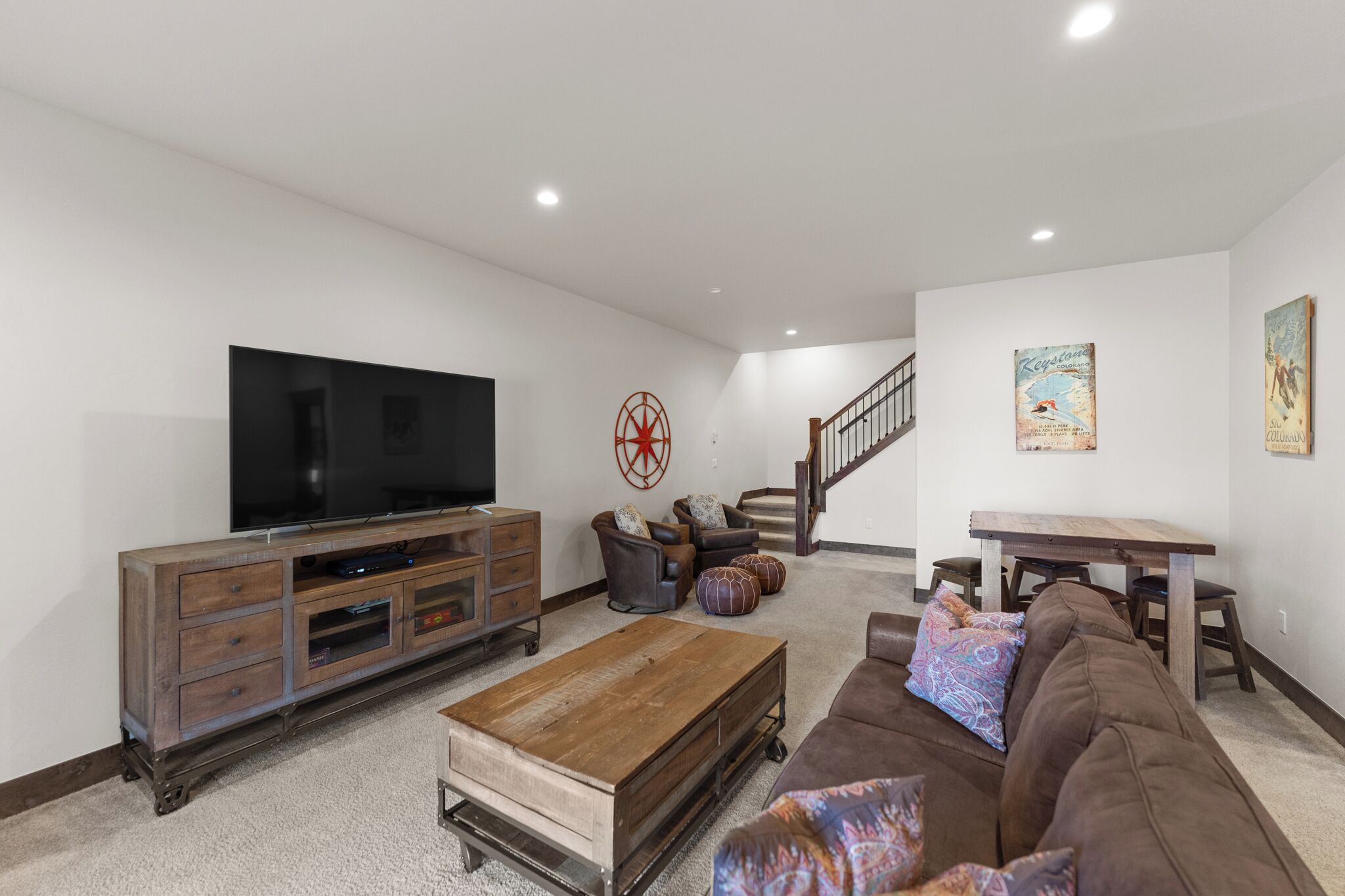 A living room with a flat-screen TV, wooden entertainment center, brown sofa, and a staircase leading to another level.