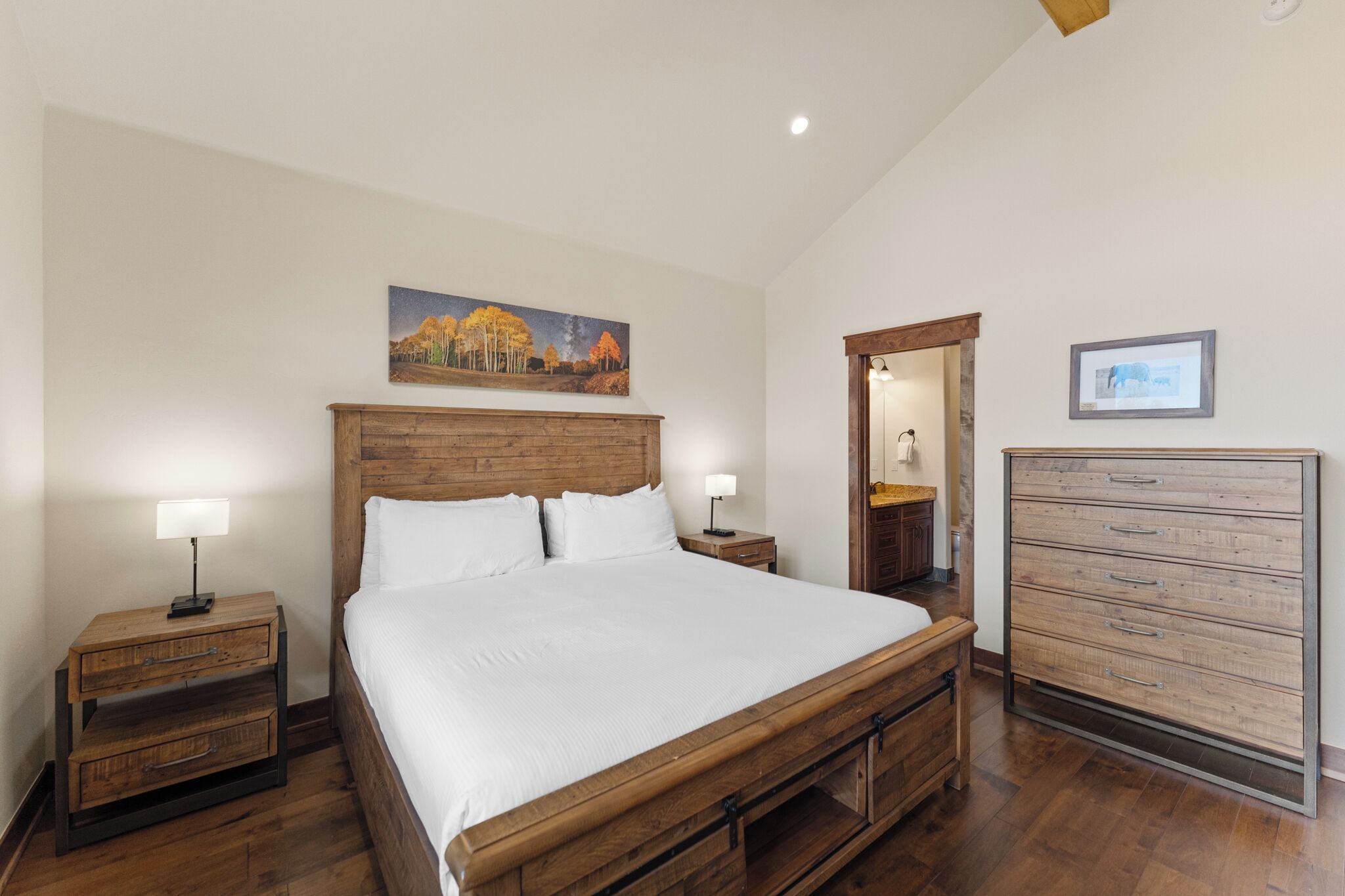A bedroom with a wooden bed, two nightstands with lamps, a dresser, and a painting on the wall.