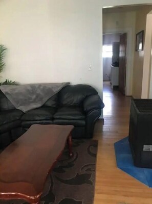 Una sala de estar con un sofá de cuero negro, una mesa de centro de madera y una alfombra azul.