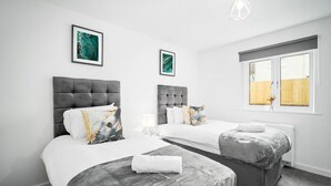 Hotellihuone, jossa on kaksi sänkyä, harmaat päätyosat, valkoiset vuodevaatteet ja taideteoksia seinillä.