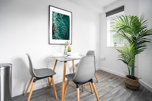 Un espace repas moderne comprenant une table, des chaises, une œuvre d’art encadrée, une plante en pot et une fenêtre donnant sur un paysage.