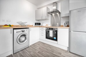 Eine moderne Küche mit weißen Schränken, einer Edelstahl-Dunstabzugshaube, einer Mikrowelle, einem Backofen und einer Waschmaschine.