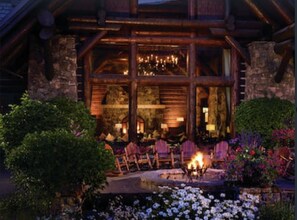 A log cabin with a stone facade, a fireplace, and outdoor seating.