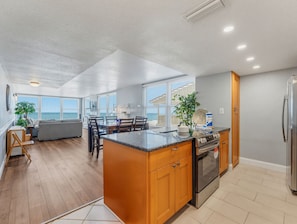 A modern kitchen with a large island, built-in oven, and refrigerator. There is a dining area with a view of the ocean.