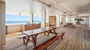 Een overdekt buitengebied met houten picknicktafels en barbecuegrills, met uitzicht op de oceaan.