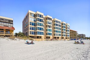 Ein Strandhotel mit mehreren Etagen, Balkonen und einem Strandabschnitt.