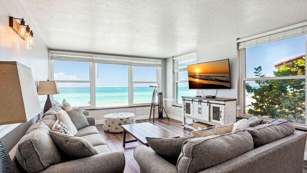 Een woonkamer met een groot raam met uitzicht op de oceaan, een flatscreen televisie en een houten salontafel.