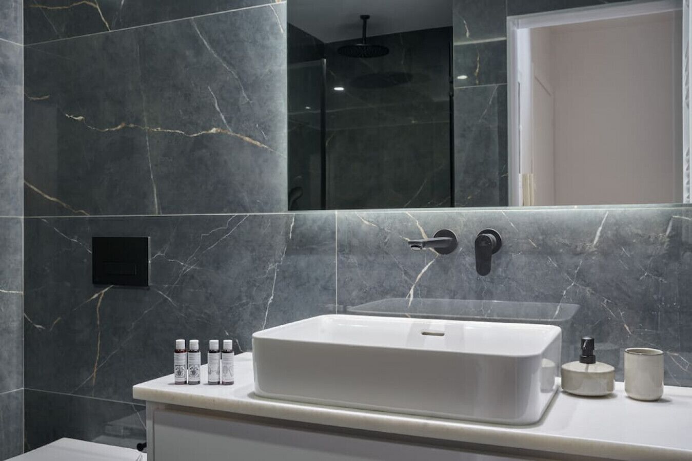 Un bagno con un lavandino bianco, pareti in marmo scuro e box doccia in vetro.