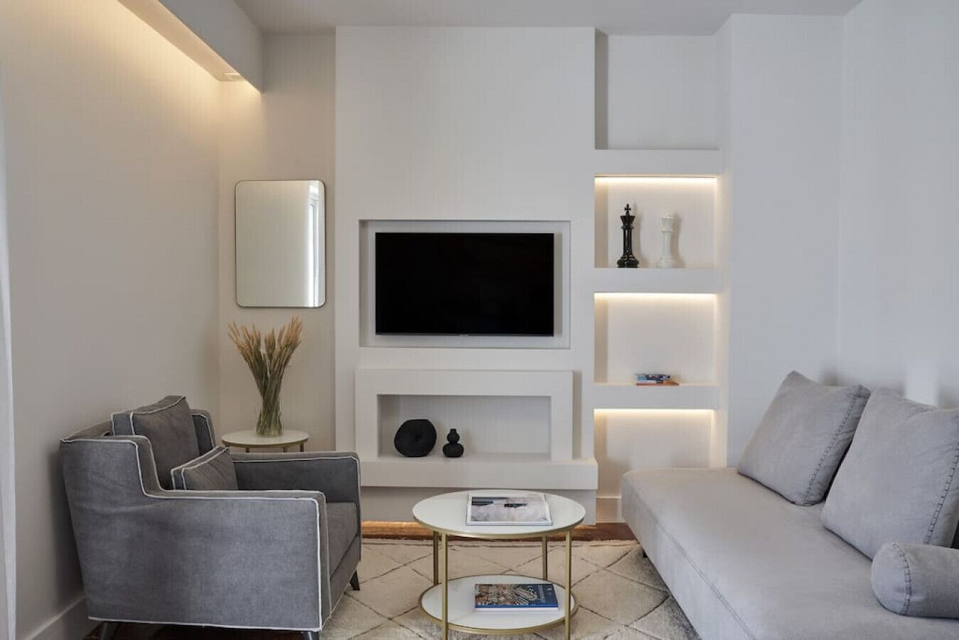 Un soggiorno moderno con una televisione a schermo piatto, divani grigi, un tavolino da caffè e scaffali decorativi.