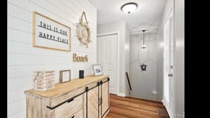 A hallway with a wooden cabinet, a sign reading "THIS IS OUR HAPPY PLACE," and a "Beach" sign. - OBX ~ Ocean Views ~ Private Pool ~ Golf Course ~ (Kitty Hawk)