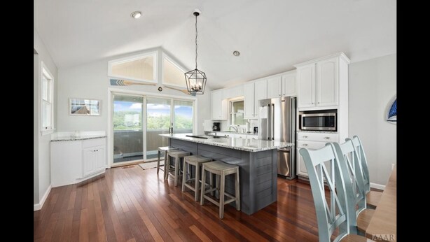 A spacious kitchen with white cabinets, a large island with stools, stainless steel appliances, and a view through the sliding glass door. - OBX ~ Ocean Views ~ Private Pool ~ Golf Course ~ (Kitty Hawk)