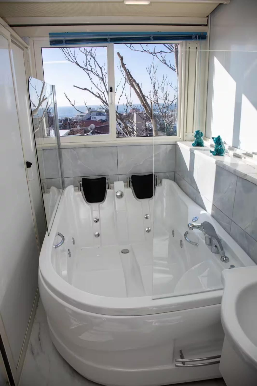 A modern bathroom with a large freestanding bathtub, a separate shower area, and a window providing a view of the cityscape.
