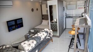 A modern living room with a grey sofa, a flat-screen TV, and a kitchen area with a bar stool. - Asparagus Hotel Suits Old City (Istanbul)