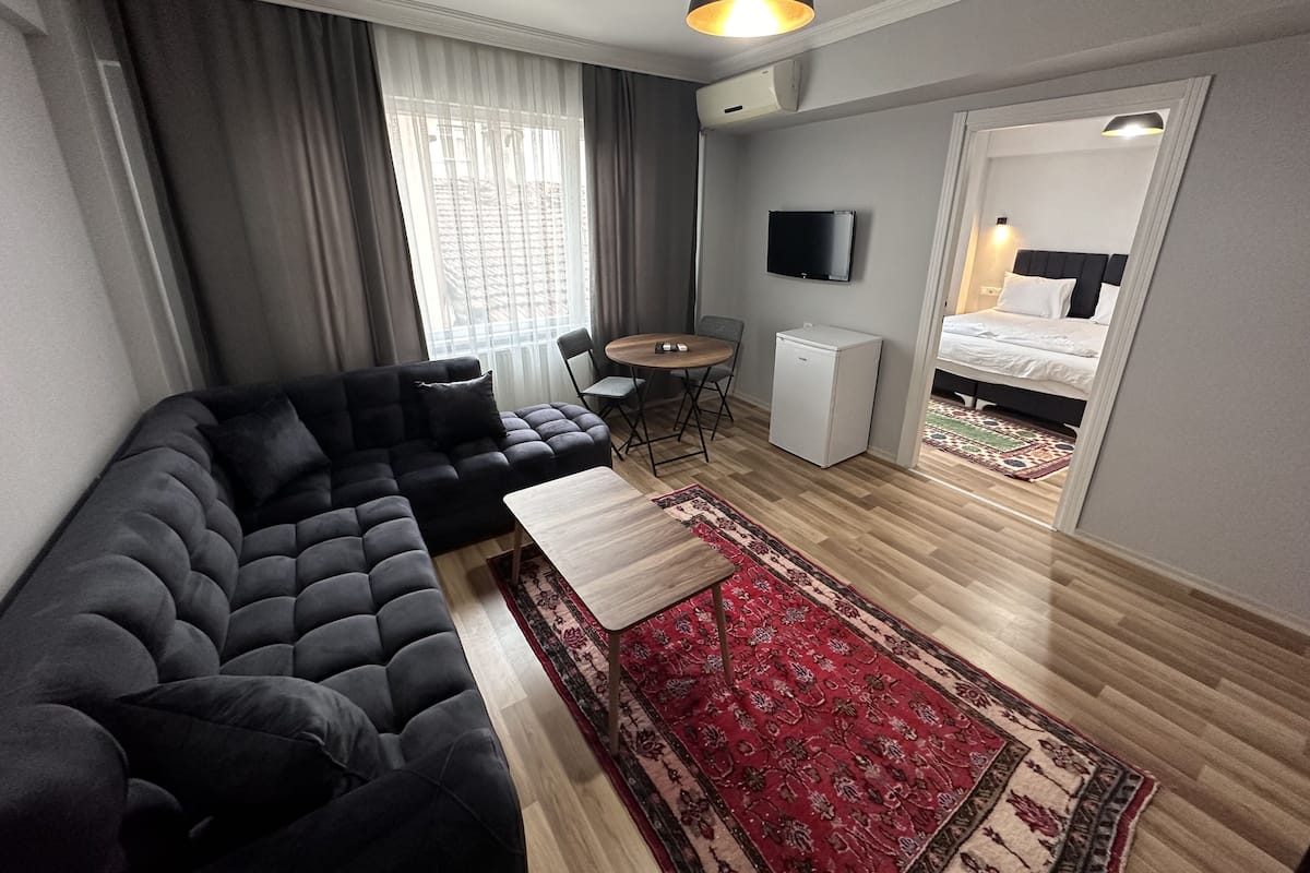 A modern living room with a black sofa, a small round table, a TV, and a compact refrigerator.
